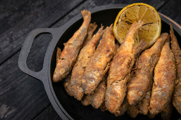 Fried fish on a black cast iron skillet on a dark wooden table
