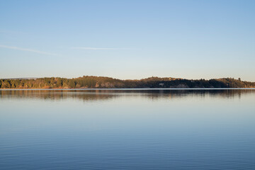 Symmetry in nature. View of the glacier water lake at sunset. The shoreline, forest and blue sky reflection in water. 