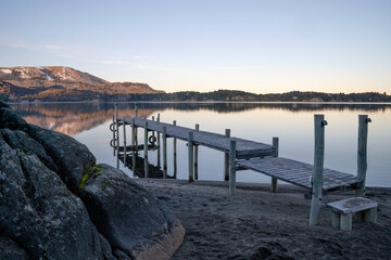 Magical view of the wooden dock in the placid lake at dusk. The mountains, forest, rocky shore and...