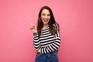 Portrait of beautiful fascinating emotional positive joyful happpy female promoter pointing to the side at copy space for advertising wearing hipster outfit isolated over background wall with empty