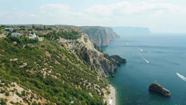 Aerial view of calm azure sea and volcanic rocky cliffs of Mys Fiolent. Pleasure trip boats moored in the bay. Nature summer ocean sea beach background. Holiday, vacation and travel concept