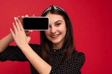 Photo of beautiful smiling girl good looking wearing casual stylish outfit standing isolated on background with copy space holding smartphone showing phone in hand with empty screen display for mockup