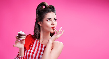 Beautiful brunette in retro style eats cake and licks her finger