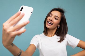 Attractive charming young smiling happy woman holding and using mobile phone taking selfie wearing...
