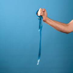 Lose weight, get rid of excess weight, a call to engage in health. A man's hand holds a centimeter ribbon in his fist, blue background