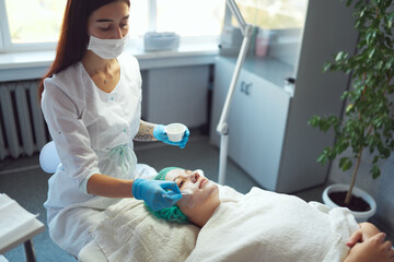 Beautician applies a moisturizing mask to the face of a young girl. Cosmetological procedure.