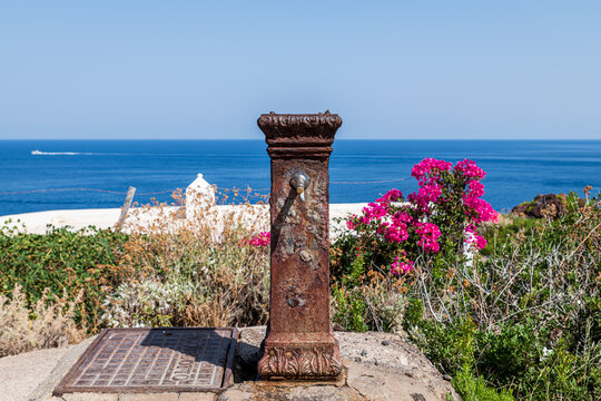 Salina island (Aeolian archipelago), Messina, Sicily, Italy, 08.17.2021: panoramic seascape  with an old drinking fountain and flowers in the foreground.