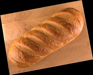 Ruddy whole loaf of bread on wood board on black background