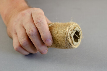 One hand holds a coil of twine against a gray background. A man shows the thin thread, which is...