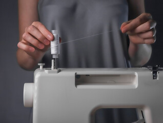 Fototapeta premium Seamstress hands putting thread spool on sewing machine close up.