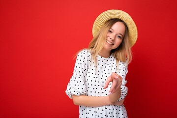 Young beautiful woman. Trendy woman in casual summer dress and straw hat. Positive female shows facial emotions. Funny model isolated on red background with free space