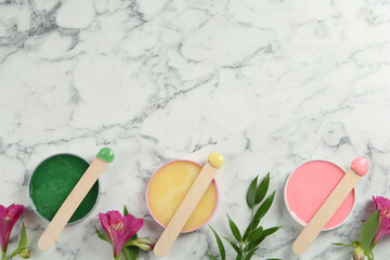 Spatula with different types of wax and flowers on white marble table, flat lay. Space for text - obrazy, fototapety, plakaty