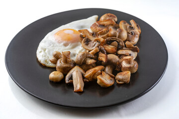 Fried champignon mushrooms with a fried egg on a black plate, isolated on white background