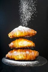 3 staked croissants sprinkled with sugar powder isolated on black
