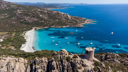 Aerial view of the ruins of the Genoese tower of Roccapina in the South of Corsica, France - Rounded tower overlooking the bay and beach of Roccapina with turquoise waters in the Mediterranean Sea - obrazy, fototapety, plakaty