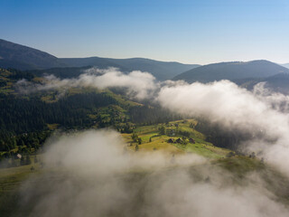 Fototapeta na wymiar A thin morning fog covers the Ukrainian mountains. Green grass on the slopes of the mountains. A curly thin fog spreads over the mountains. Aerial drone view.