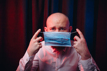 Man in white shirt putting on blue gauze mask. Emotion of fear and pain. Healthcare, respiratory illness prevention, prophylaxis of virus infections, COVID-19 concept.