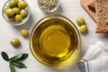 Glass bowl with fresh olive oil on white wooden table, flat lay