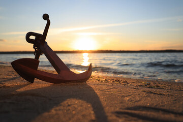 Wooden anchor on shore near river at sunset - obrazy, fototapety, plakaty