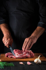 The chef cuts meat with a knife in the kitchen prepares food. Vegetables and spices on the kitchen table in a restaurant to prepare a delicious lunch