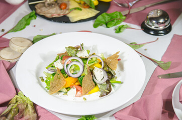 salad with vegetables and cheese with crackers in a white plate on the table with a white tablecloth and pink napkins decorated for Christmas