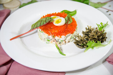 winter salad, olivier, with red caviar in a white round plate on the table with a white tablecloth and pink napkins decorated for Christmas