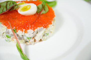 winter salad, olivier, with red caviar in a white round plate on the table with a white tablecloth and pink napkins decorated for Christmas close up