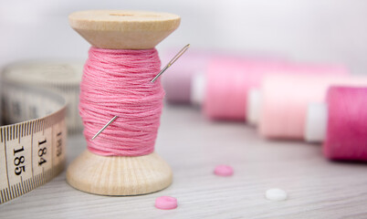 A spool of pink thread, a cloth and a needle on a wooden table. Sewing accessories - Powered by Adobe