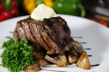 beef steak with fried mushrooms on a side dish on a white plate on a wooden board