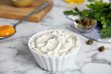 Tasty tartar sauce and ingredients on white marble table