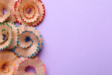 Colorful wooden pencil shavings on violet background, flat lay. Space for text
