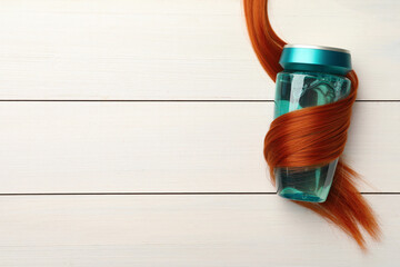 Bottle wrapped in lock of hair on white wooden background, top view with space for text. Natural cosmetic product