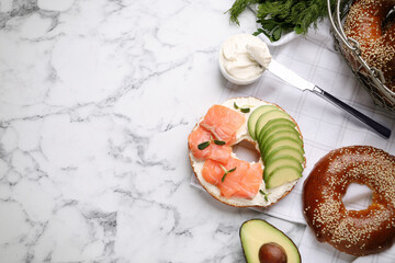 Delicious bagel with cream cheese, salmon and avocado on white marble table, flat lay. Space for...
