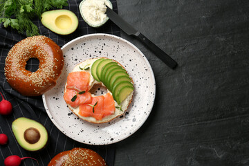 Delicious bagel with cream cheese, salmon and avocado on black table, flat lay. Space for text