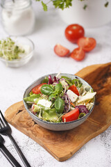 A small white salad bowl with microgreens, cherry tomatoes and fresh basil leaves on a wooden board on a grey concrete surface