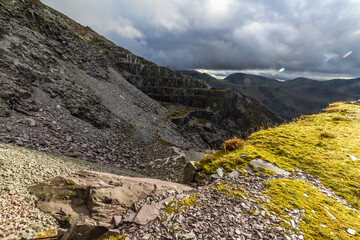 Sunlight and shadow over high slate quarry, mountains behind, landscape.