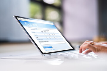 Businessperson's Hand Filling Online Survey Form On Laptop