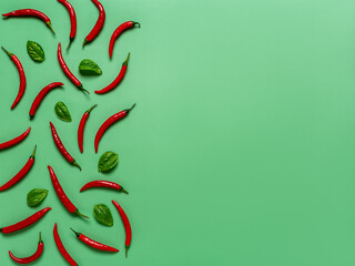 Raw red hot chili peppers and fresh basil leaves on an emerald green background. Spicy chilli pepper pods creative composition for food design. Blank mock up with copy space for menu. Flat lay. 
