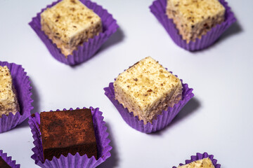 Various chocolate pralines candies in purple molds highlighted on a white background. Top view. The...