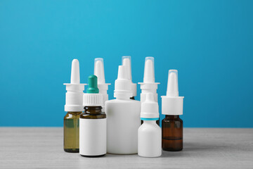 Nasal sprays in different bottles on white wooden table against light blue background