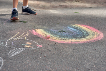 Kids paint outdoors. Boy drawing a rainbow colored chalk on the asphalt the playground