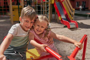 Fototapeta na wymiar Kids play on the playground. Happy laughing boy and girl have fun swinging and climbing outdoor