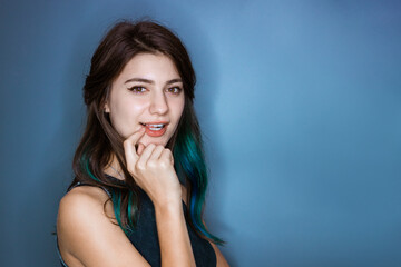 Surprised tender young woman of 20s holding finger at mouth open isolated on blue background studio portrait. With a mysterious pensive expression flirts