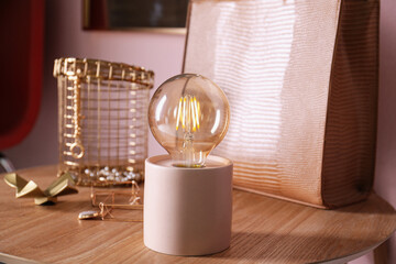 Modern night lamp, stylish bag and decor on wooden table indoors