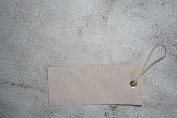 a beige rectangular tag from clothes with a thread lies on a gray background. top view