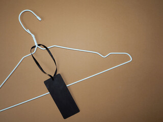 a white metal hanger with a black clothing tag lies on a brown background. top view