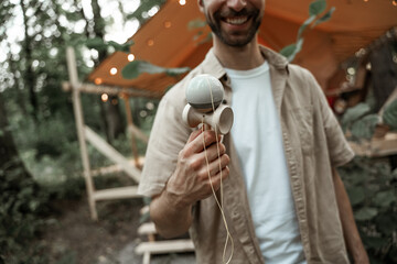 Young smiling man with stubble enjoy playing kendama at camping site, traditional skill toy....