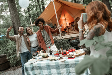 Red-haired young woman making polaroid photo of her friends on picnic, camping glamping life, resting with diverse friends outdoors, enjoying summer camping trip, having fun time in forest, copy space