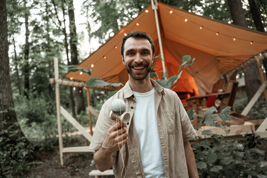 Young smiling man with stubble enjoy playing kendama at camping site, traditional skill toy. Cup-and-ball game. Wooden toy. Millennial with japanees toy entertaining friends in summer glamping