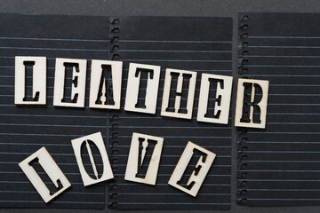 the expression "leather love" in wooden stencil font on black notepaper